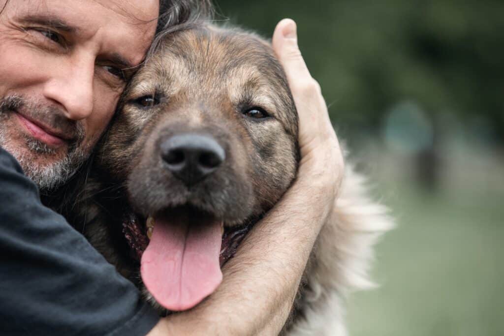 A Middle-Aged Man Hugs A Dog On A Walk